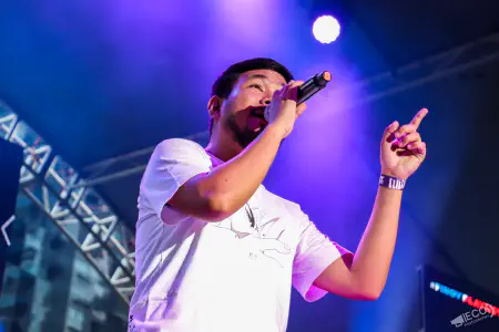 Pael singing into a microphone and pointing upward under blue and purple stage lights