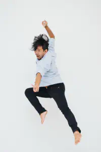 Pael jumping barefoot with one arm raised against a white backdrop