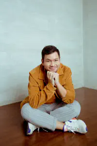 Pael sitting cross-legged in a corduroy jacket with his chin resting on his hands