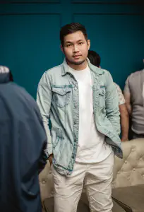 Pael standing in a denim jacket in front of a teal wall