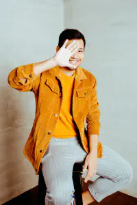 Pael smiling with one hand raised beside his face in a corduroy jacket